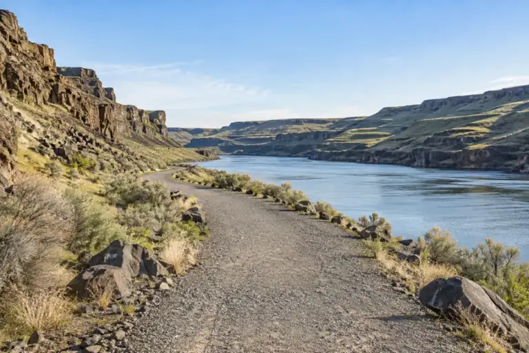 Sendero de grava Columbia Plateau junto al río Snake, con acantilados basálticos y artemisas.